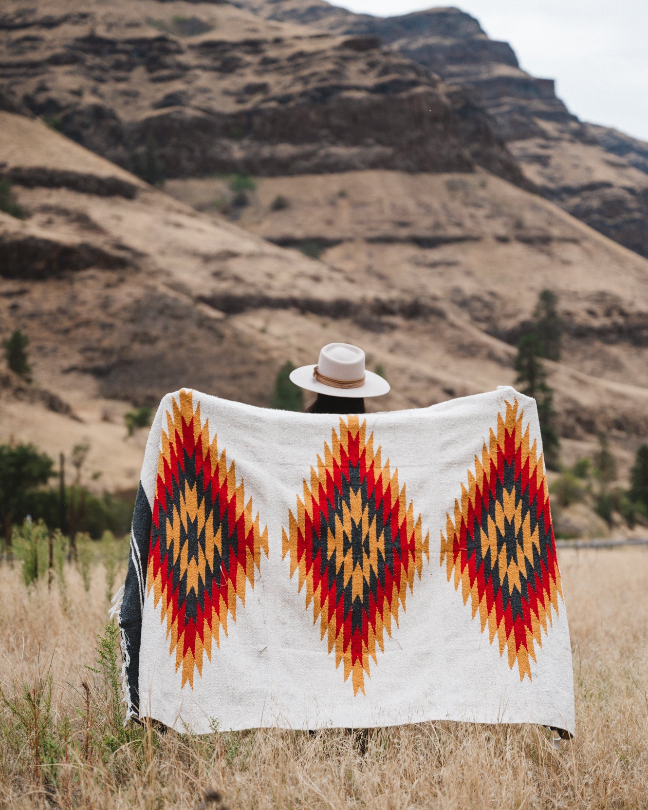 Woman holding up southwestern style diamond blanket in the high desert