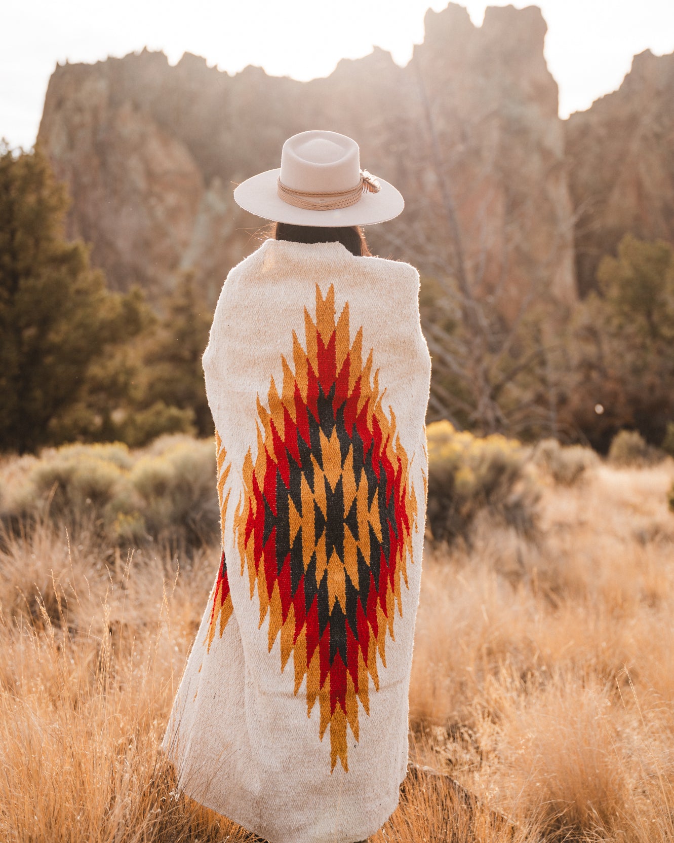 Woman wearing cowboy hat wrapped in southwestern style diamond blanket in the desert