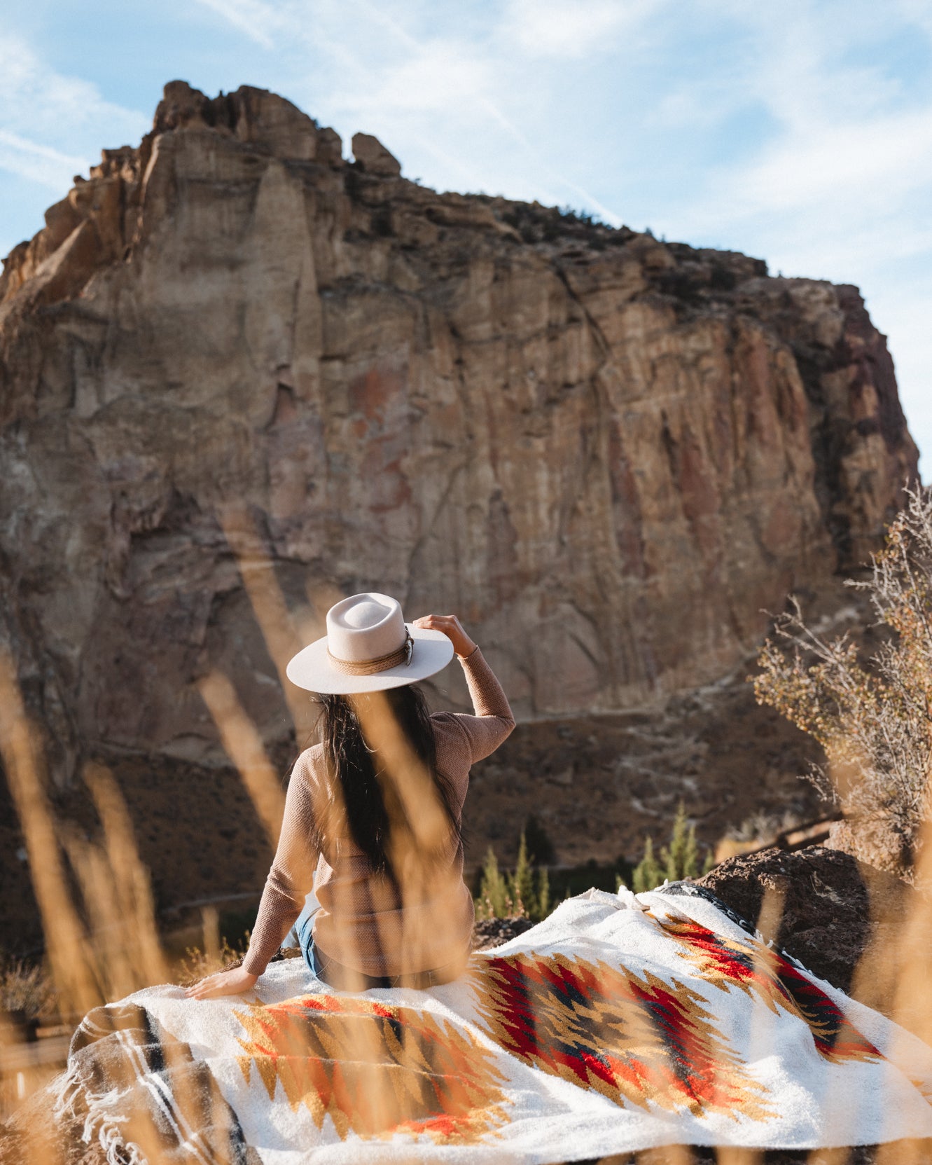 Woman sitting on southwestern style blanket in the desert wearing a cowboy hat
