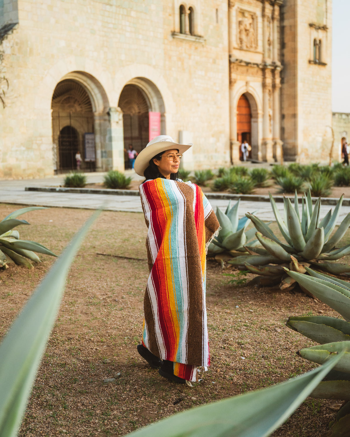 Santo Domingo Church Oaxaca and a girl standing with a handwoven mexican blanket in front of it