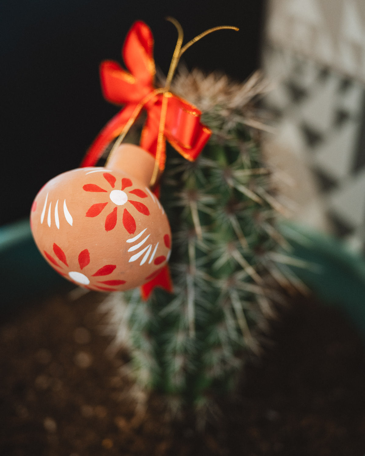 Decorative oval christmas decoration with floral pattern and red ribbon hanging on a cactus plant.
