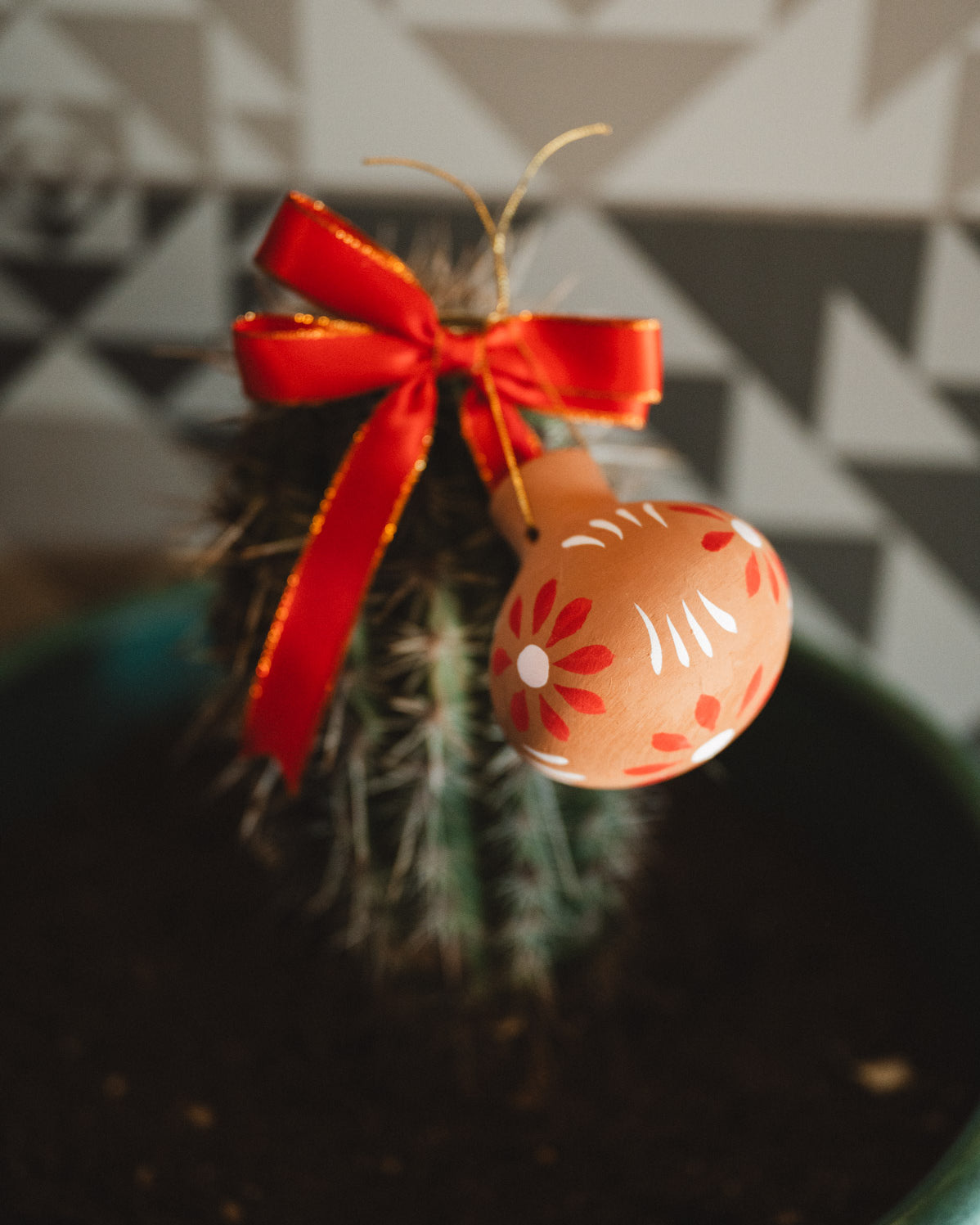 Decorative oval christmas decoration with floral pattern and red ribbon hanging on a cactus plant.