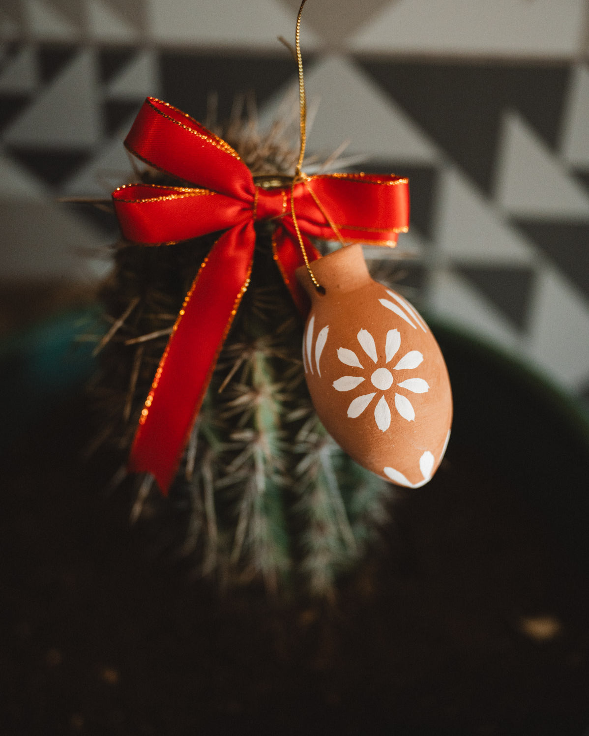 Decorative oval christmas decoration with floral pattern and red ribbon hanging on a cactus plant.