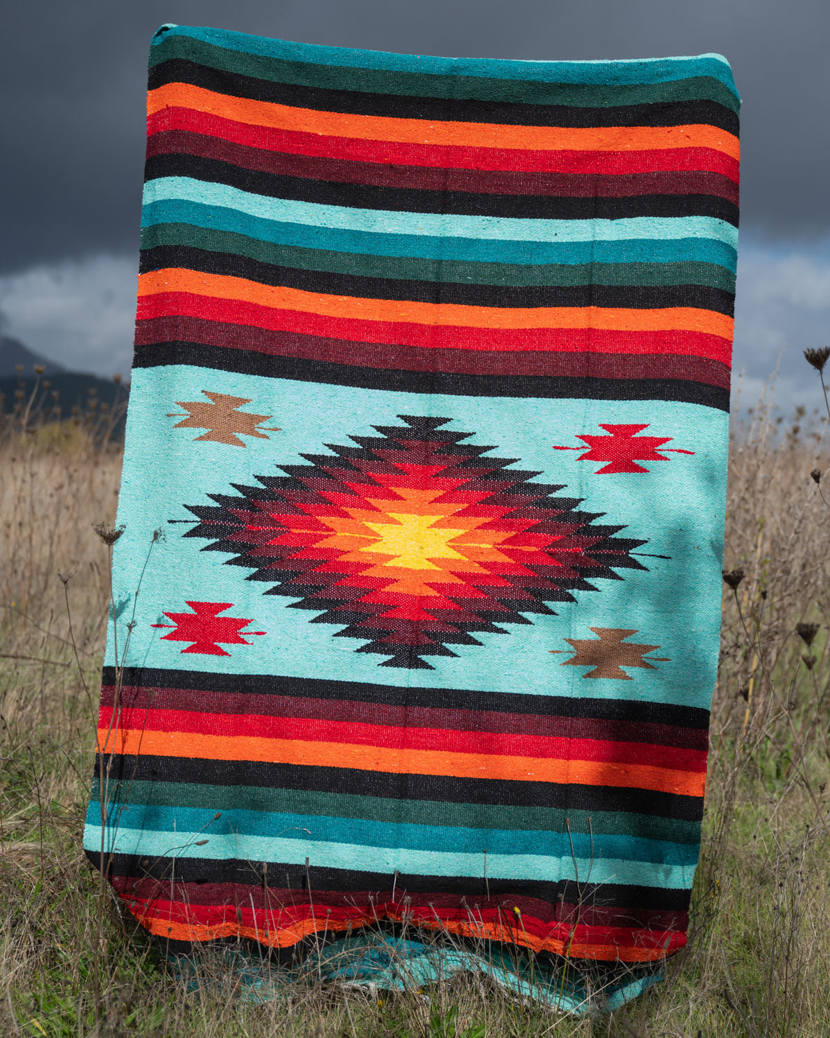Teal and red handwoven mexican blanket being held up in a field