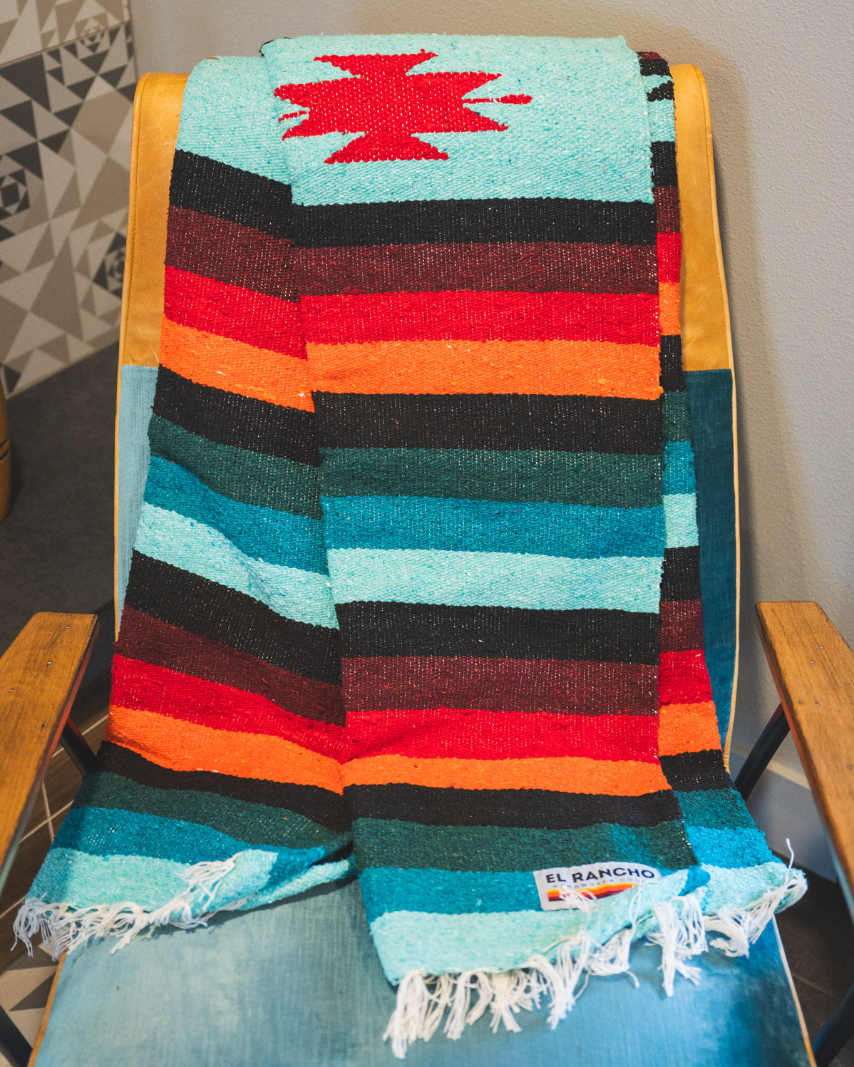 Teal and orange handwoven diamond zapatec blanket laying on a chair in a living room