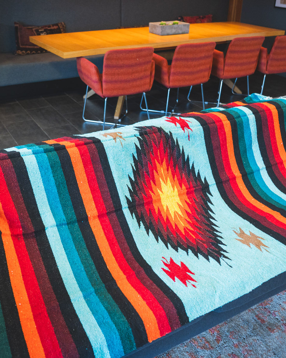 Teal and orange handwoven diamond zapatec blanket laying on a couch in a living room