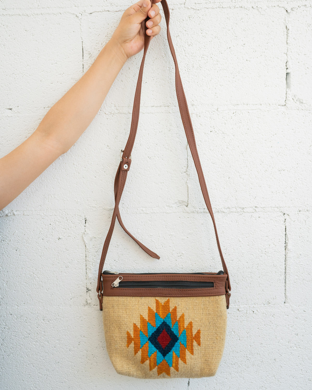 Gold and blue Mexican handbag being held against a white brick wall by an arm