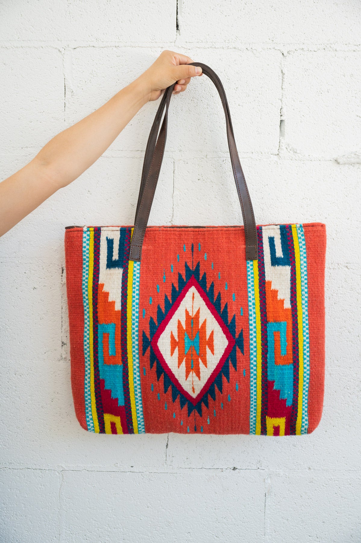 Red Mexican handbag being held up by an arm against a white brick wall