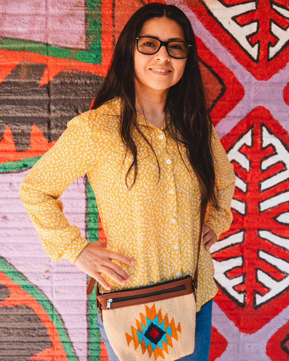 Mexican woman standing in front of colorful wall wearing a handwoven wool purse from teotitlan del valle oaxaca