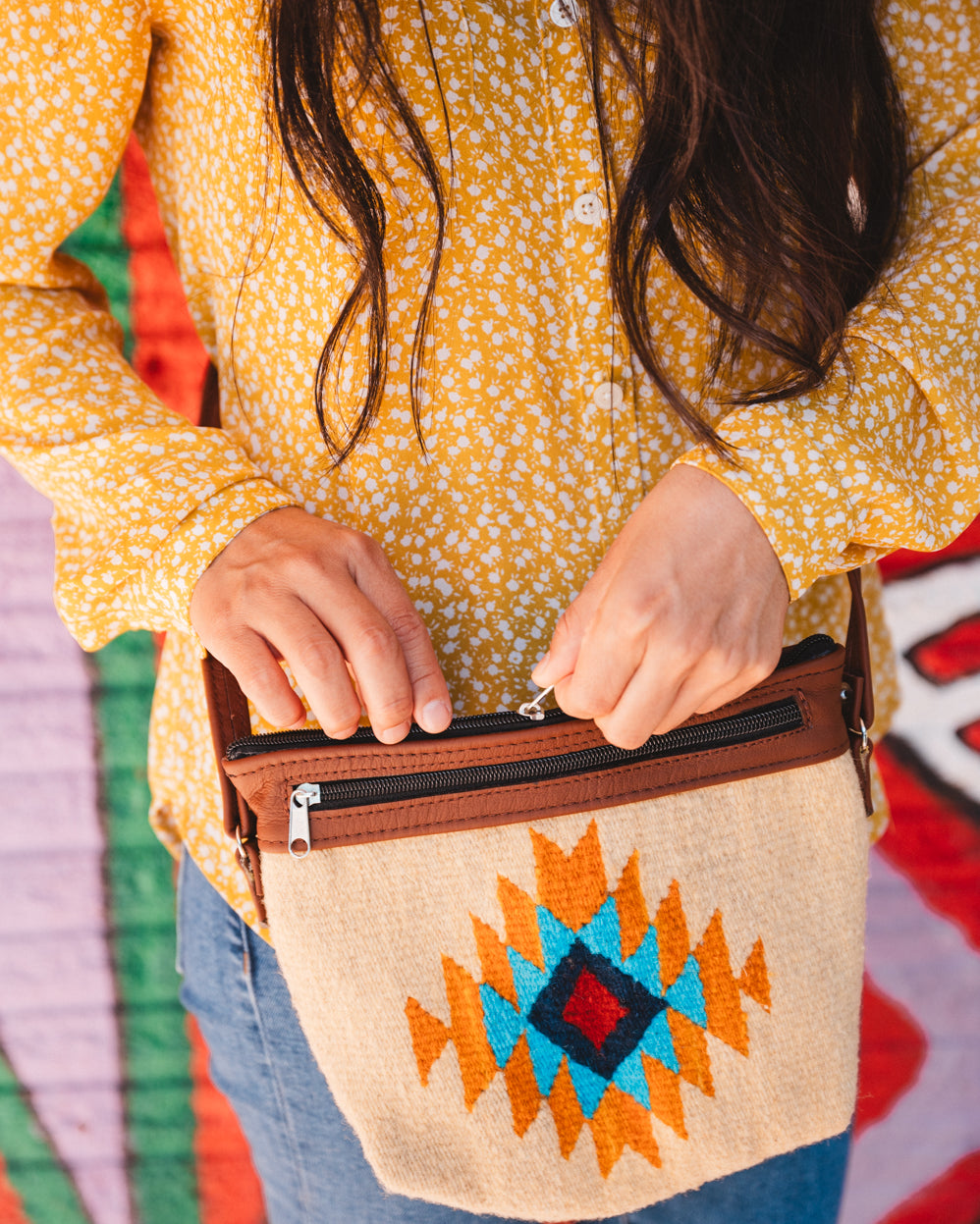 Mexican woman standing in front of colorful wall wearing a handwoven wool purse from teotitlan del valle oaxaca