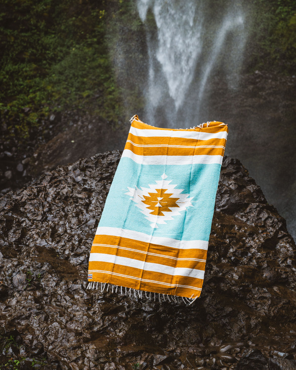 turquoise and gold mexican blanket in front of a waterfall