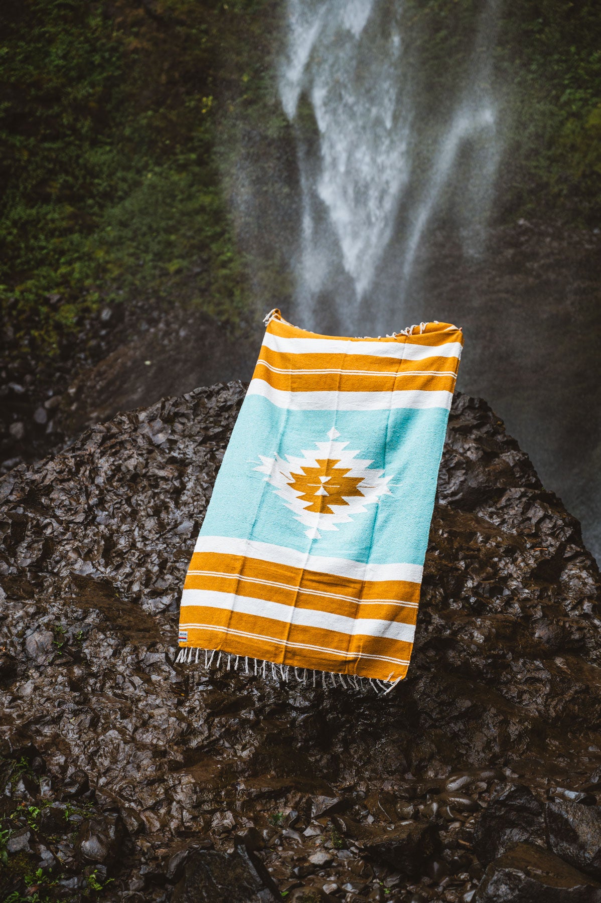 turquoise and gold mexican blanket in front of a waterfall