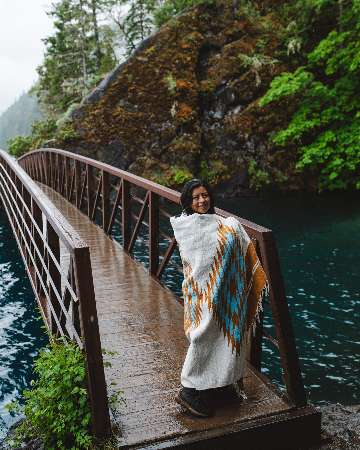 Woman in the olympic peninsula PNW wrapped in a turquoise and gold handwoven mexican diamond blanket
