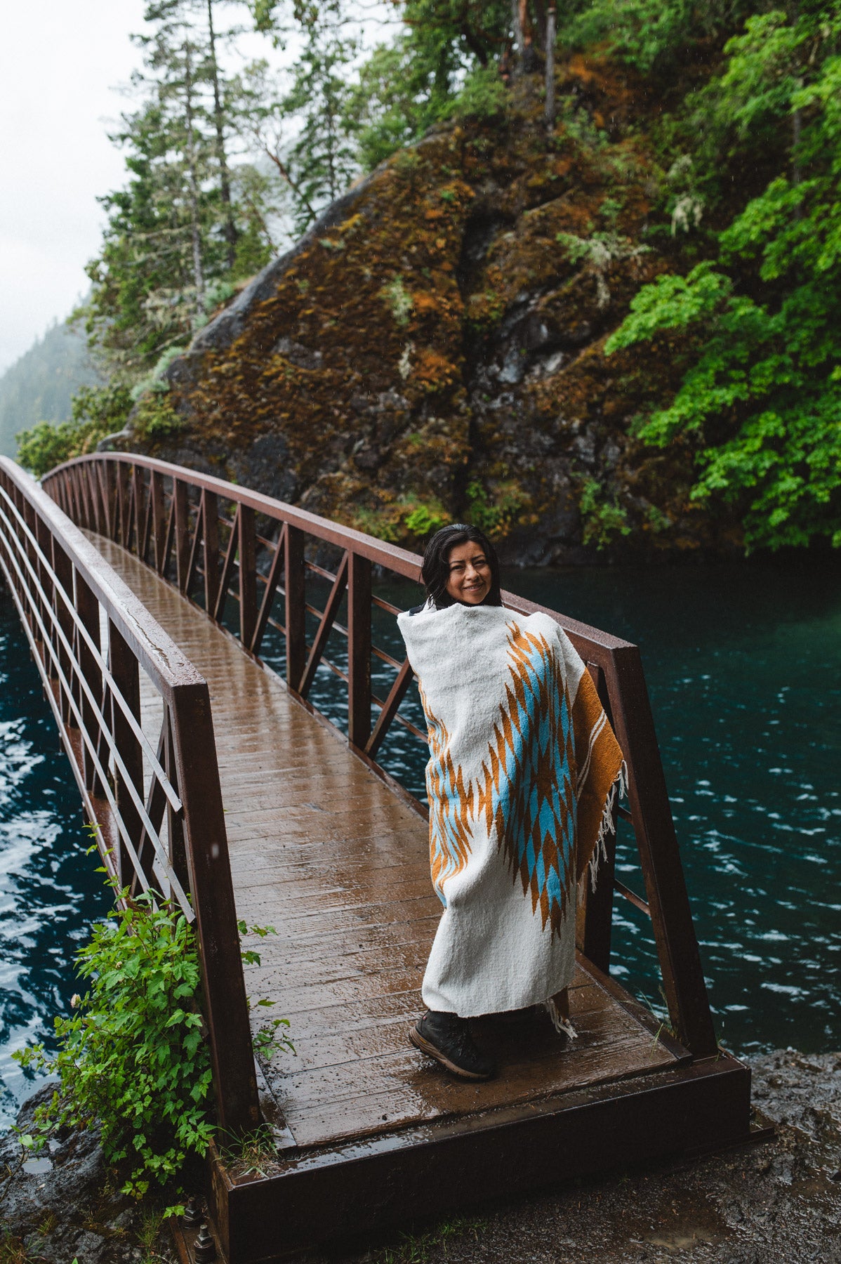 Woman in the olympic peninsula PNW wrapped in a turquoise and gold handwoven mexican diamond blanket