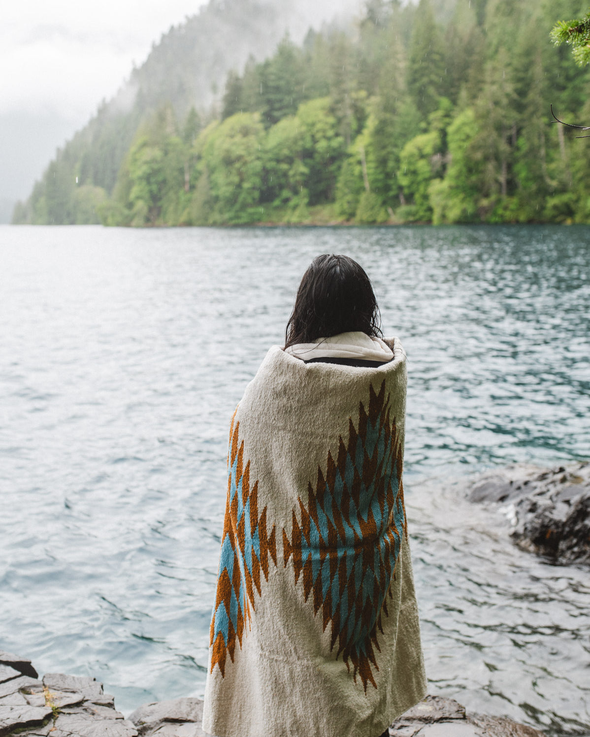Woman in the olympic peninsula PNW wrapped in a turquoise and gold handwoven mexican diamond blanket