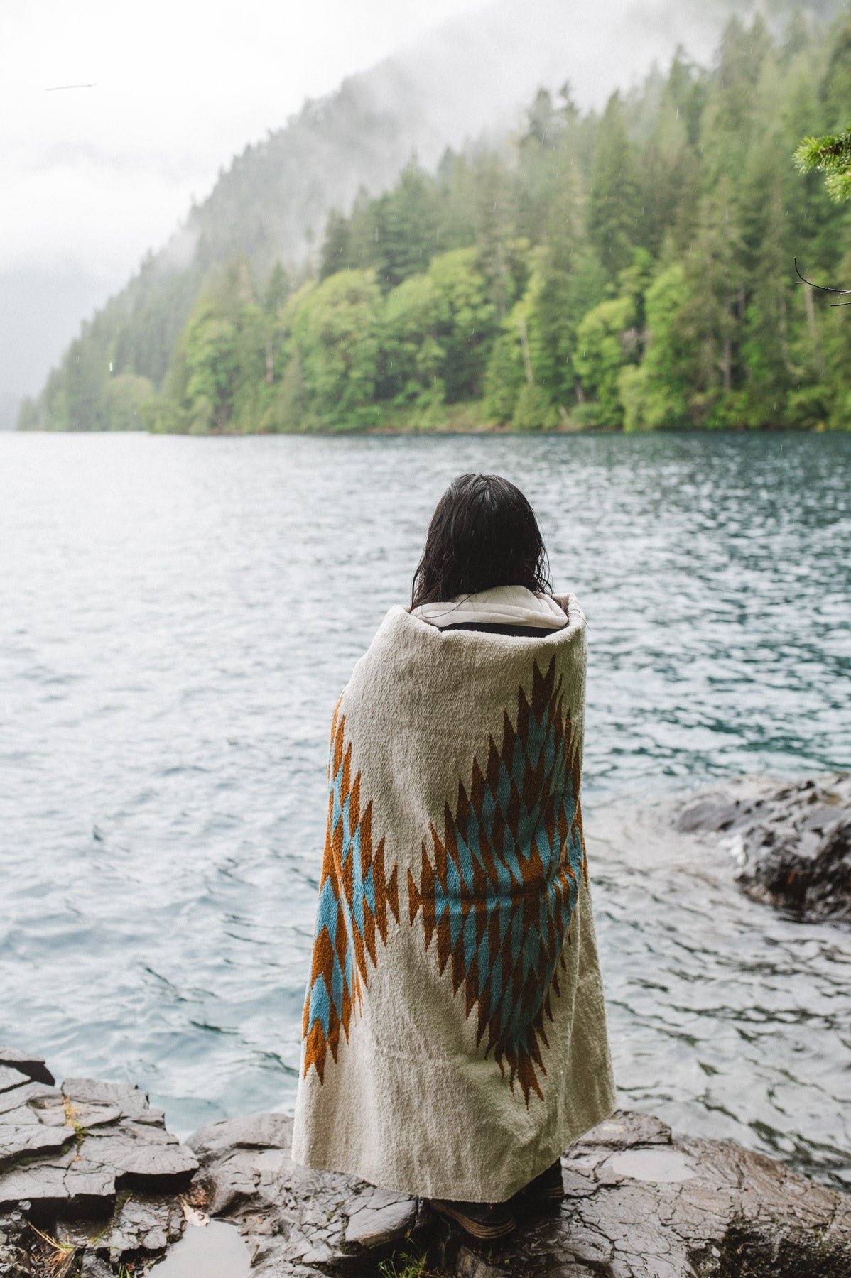 Woman in the olympic peninsula PNW wrapped in a turquoise and gold handwoven mexican diamond blanket