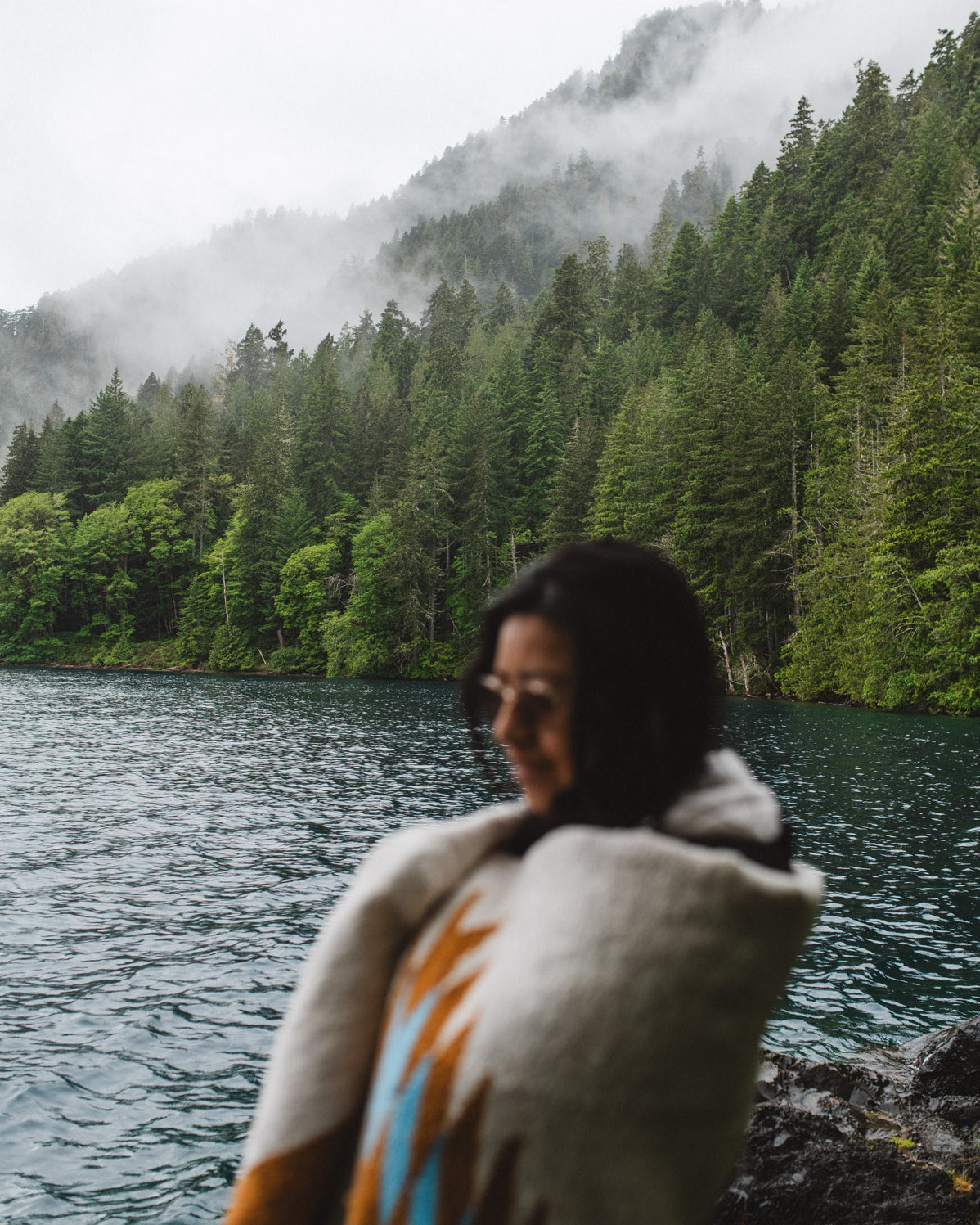 Woman in the olympic peninsula PNW wrapped in a turquoise and gold handwoven mexican diamond blanket