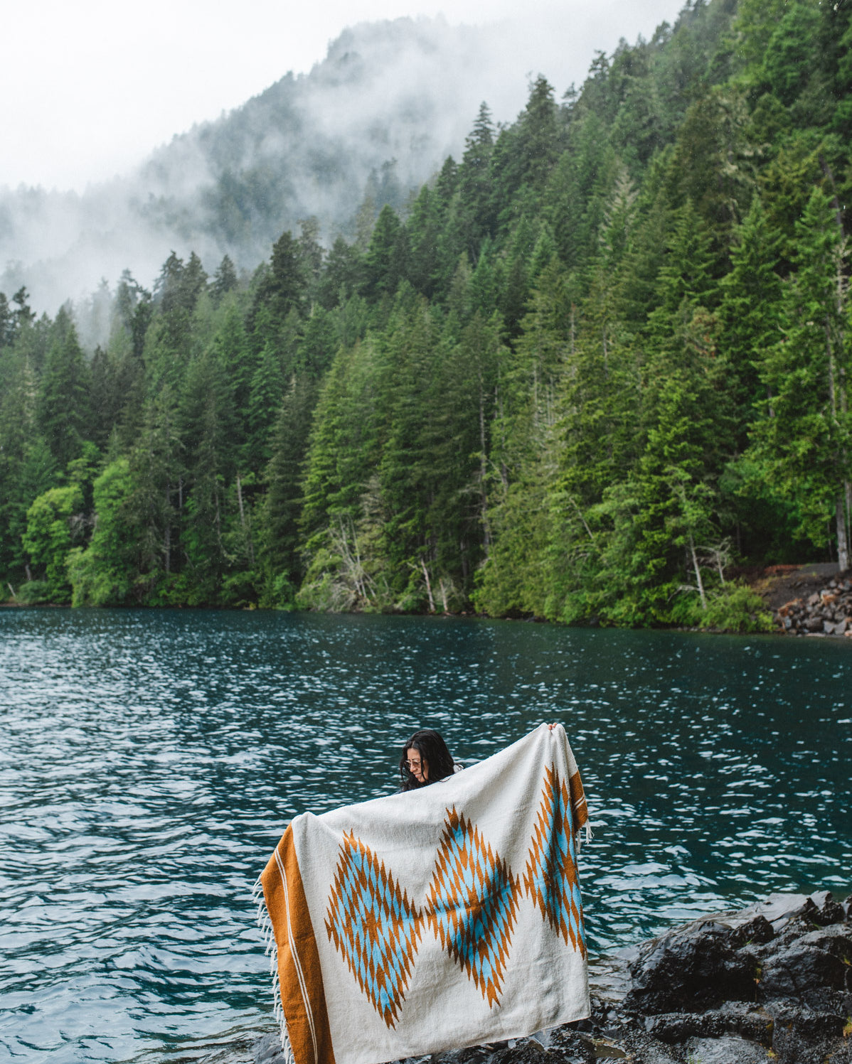 Woman in the olympic peninsula PNW wrapped in a turquoise and gold handwoven mexican diamond blanket