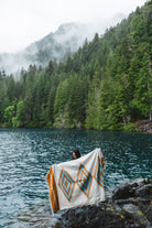 Woman in the olympic peninsula PNW wrapped in a turquoise and gold handwoven mexican diamond blanket