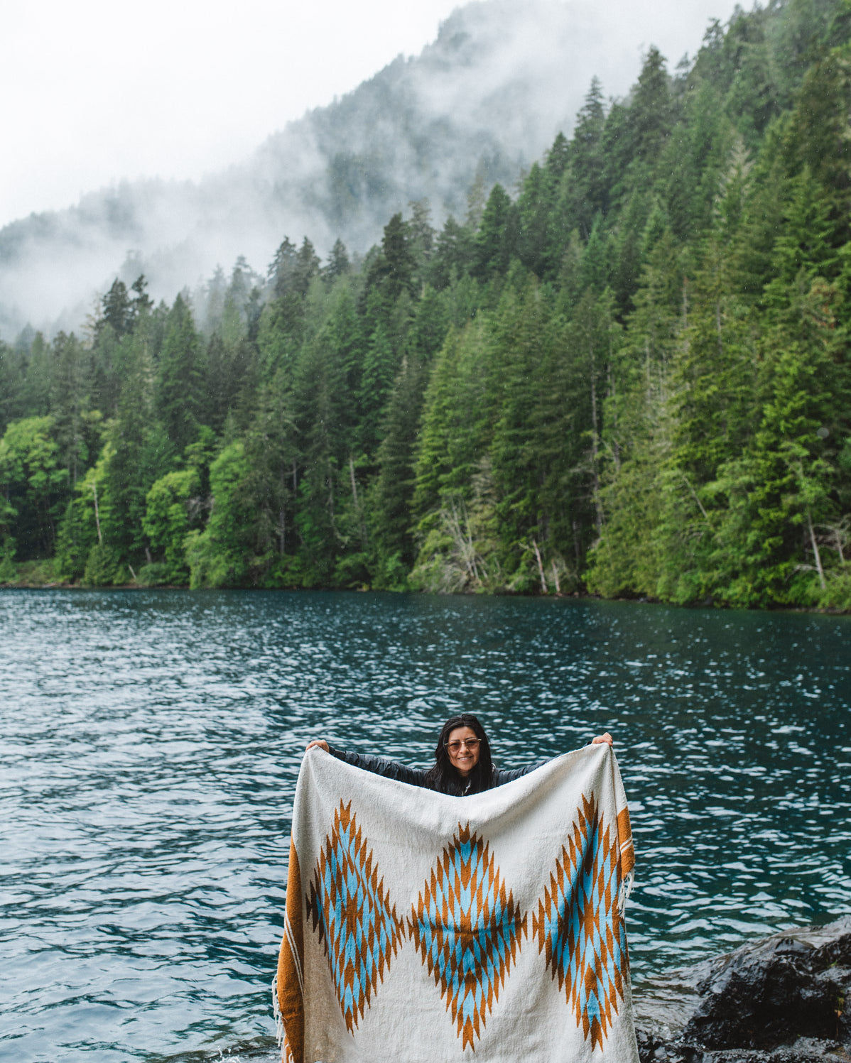 Woman in the olympic peninsula PNW wrapped in a turquoise and gold handwoven mexican diamond blanket