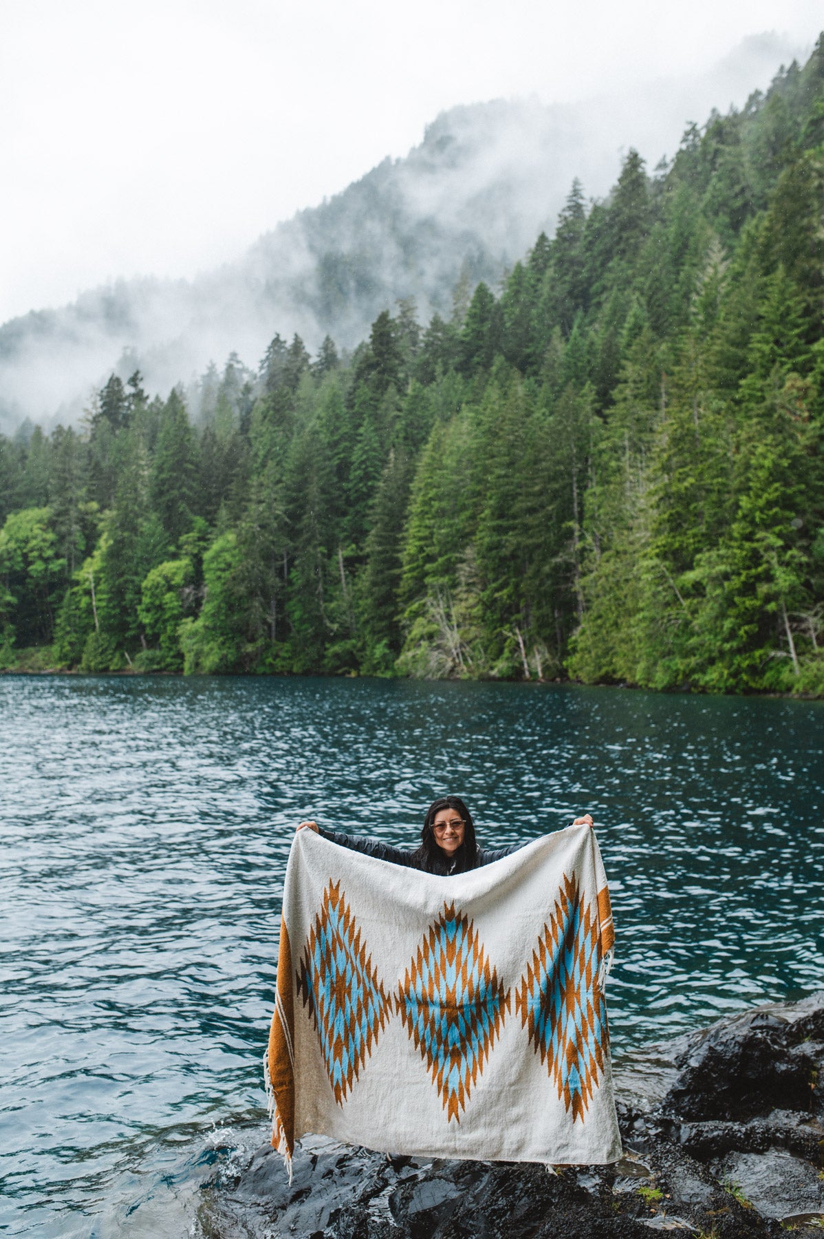 Woman in the olympic peninsula PNW wrapped in a turquoise and gold handwoven mexican diamond blanket