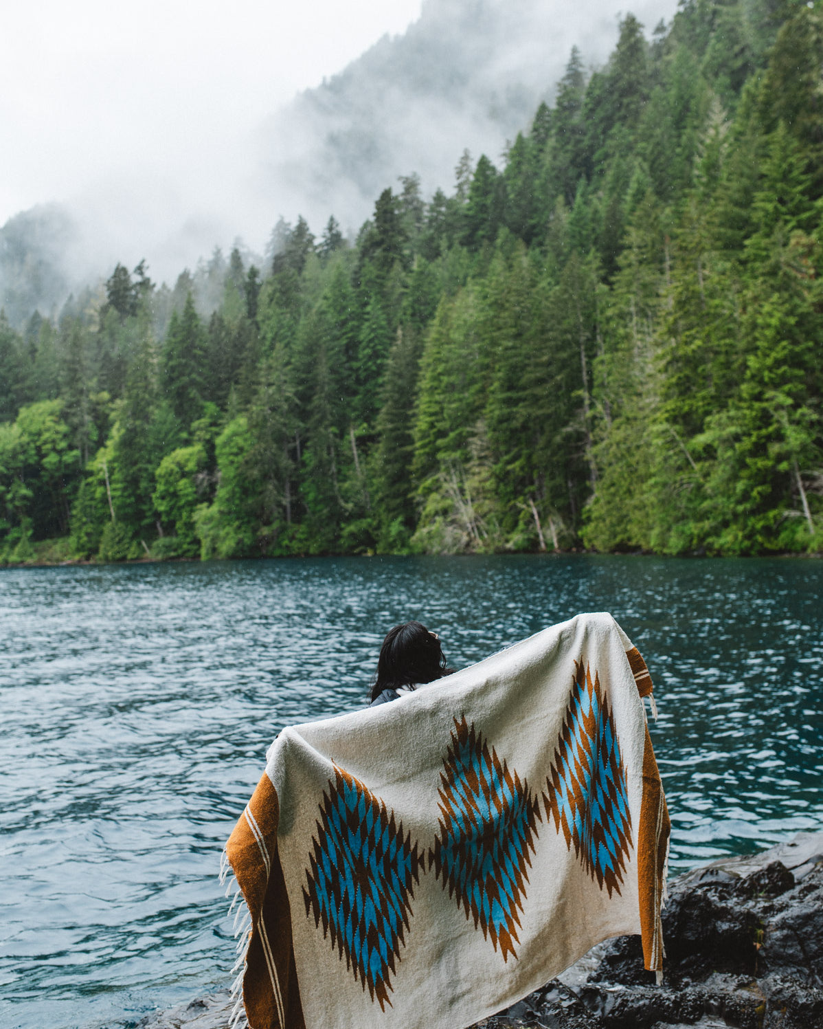 Woman in the olympic peninsula PNW wrapped in a turquoise and gold handwoven mexican diamond blanket