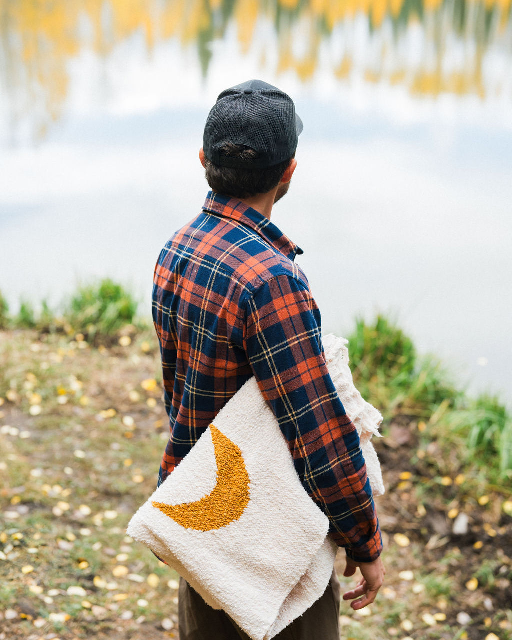 man holding a folded blanket in front of a lake