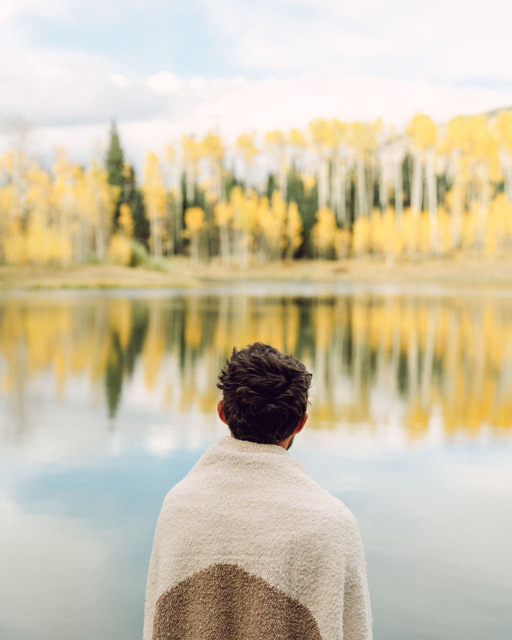 Man wrapped in tan blanket standing in front of a lake