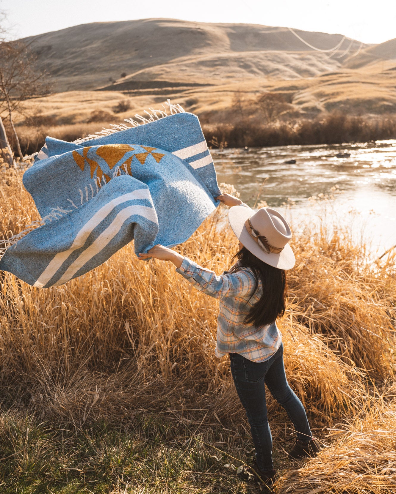 Woman throwing a blue blanket in the air in a field at sunset in the high desert