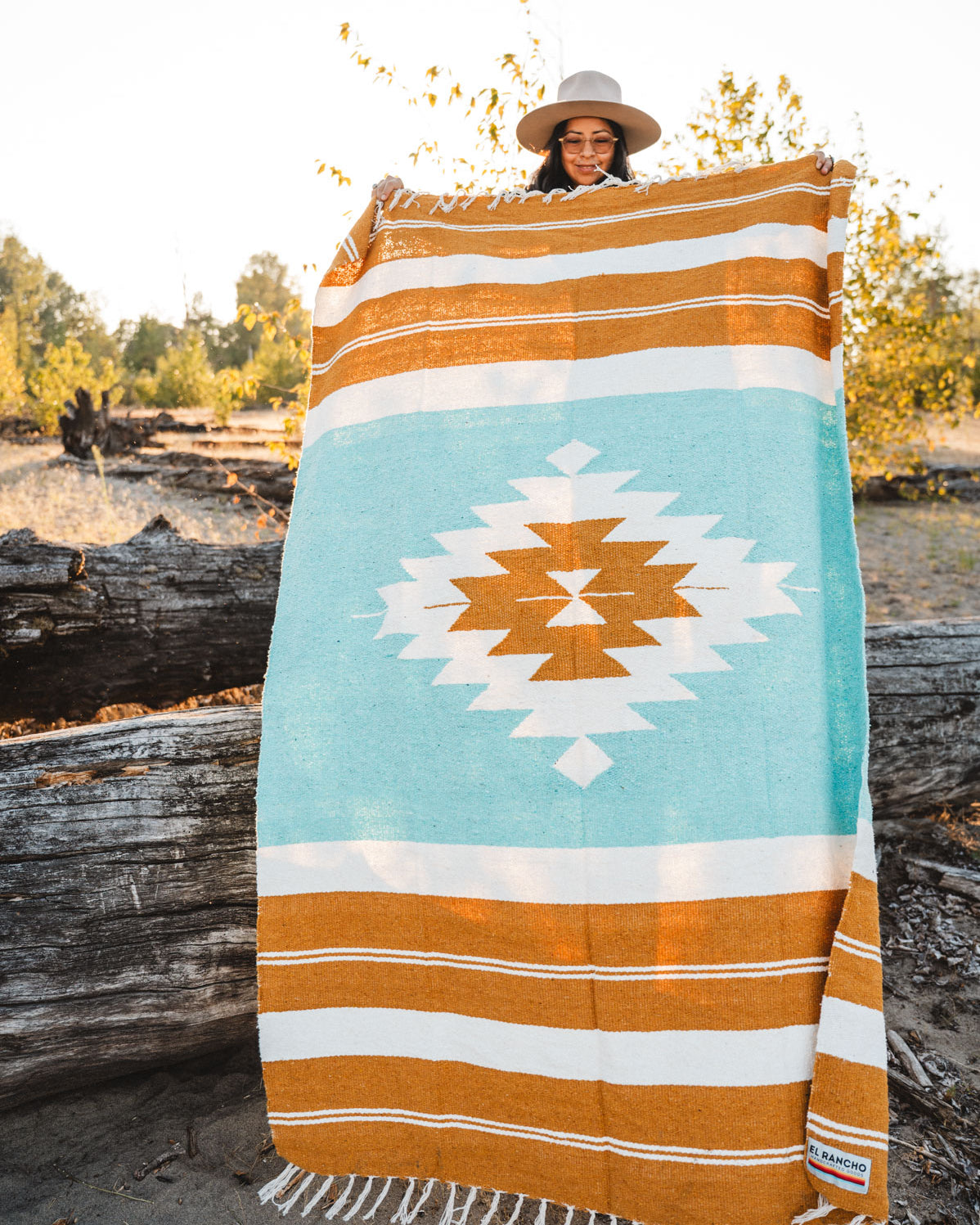 Person holding gold and turquoise handwoven mexican blanket