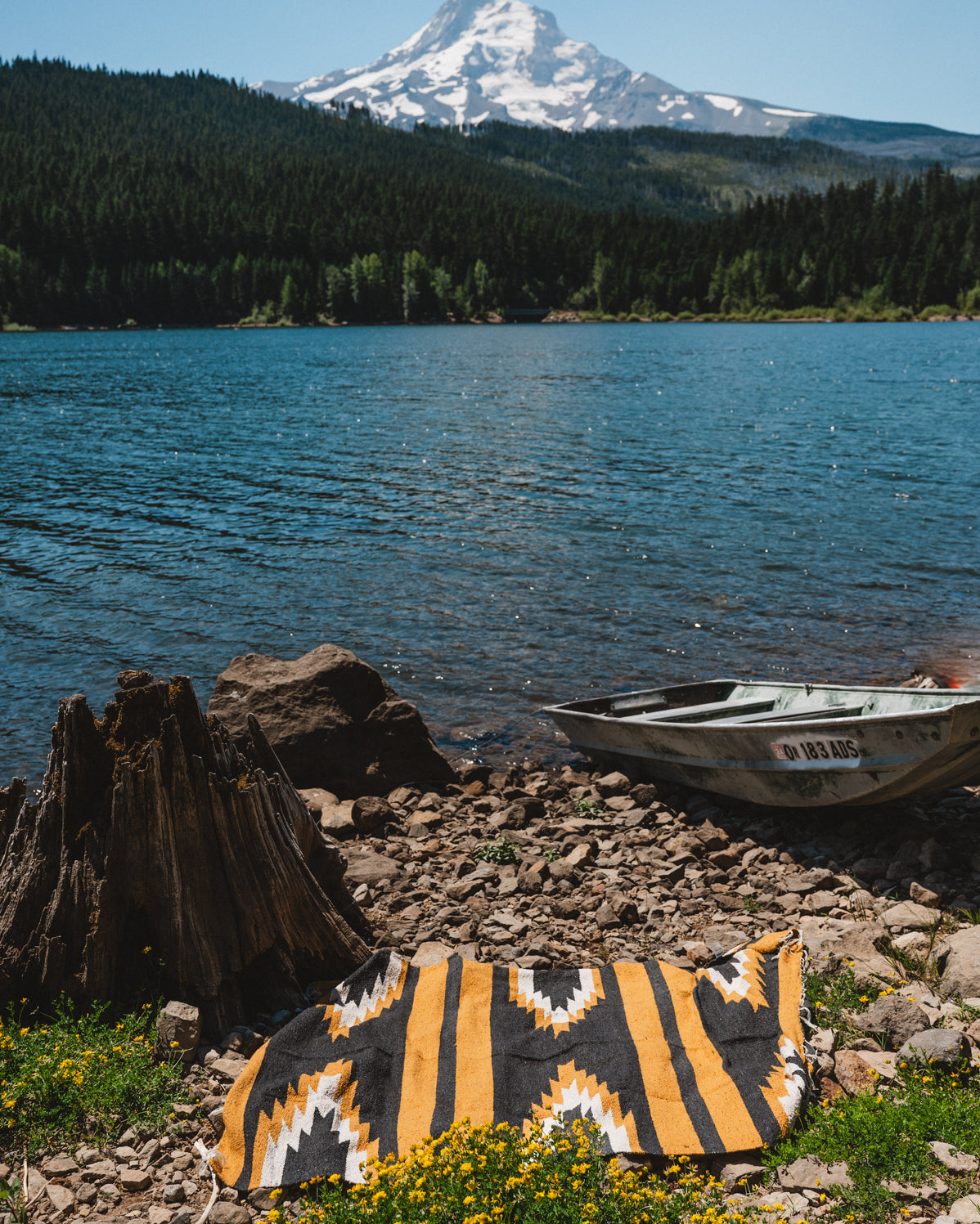 Yellow and black relampago zapotec blanket on ground  in front of mountain lake