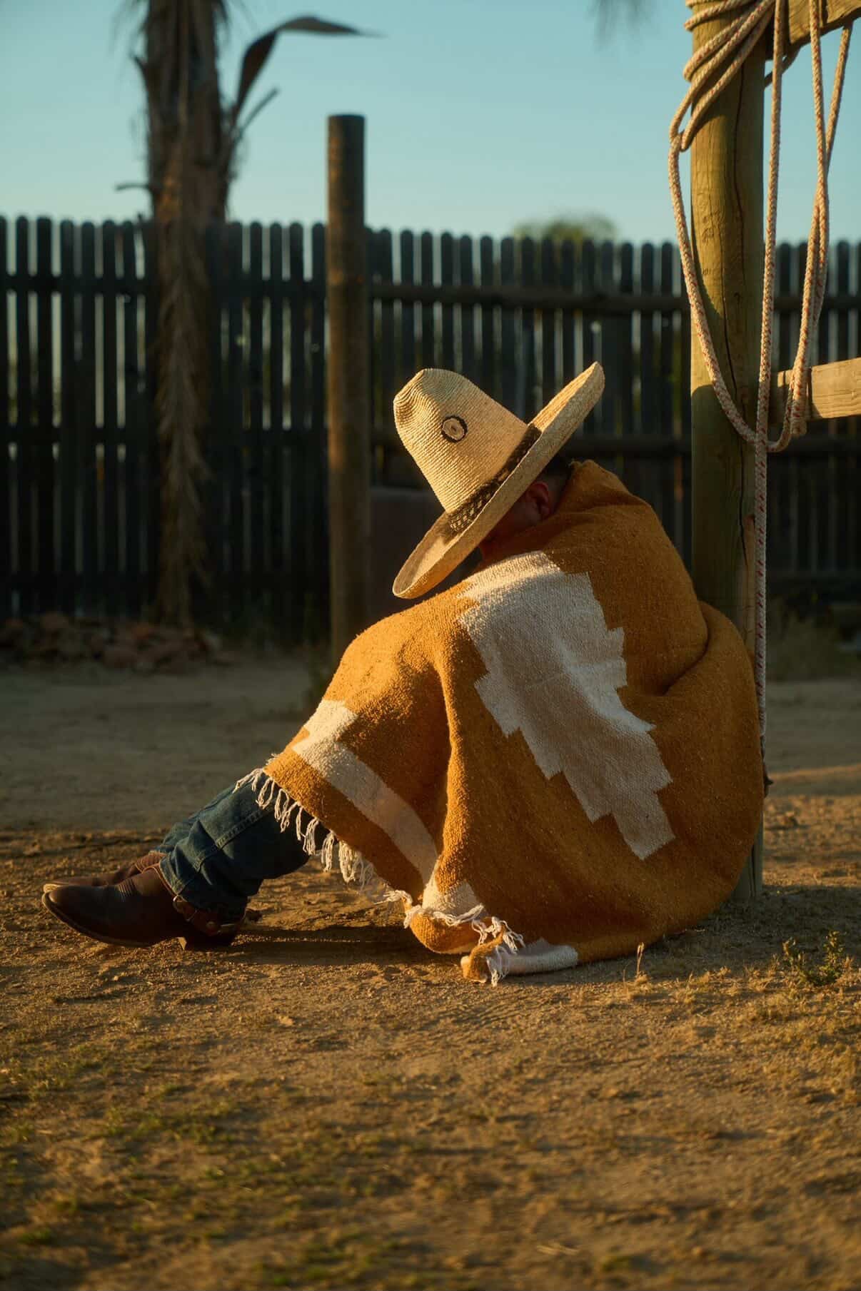 Man in sombrero wearing old handwoven mexican blankt sitting on the ground