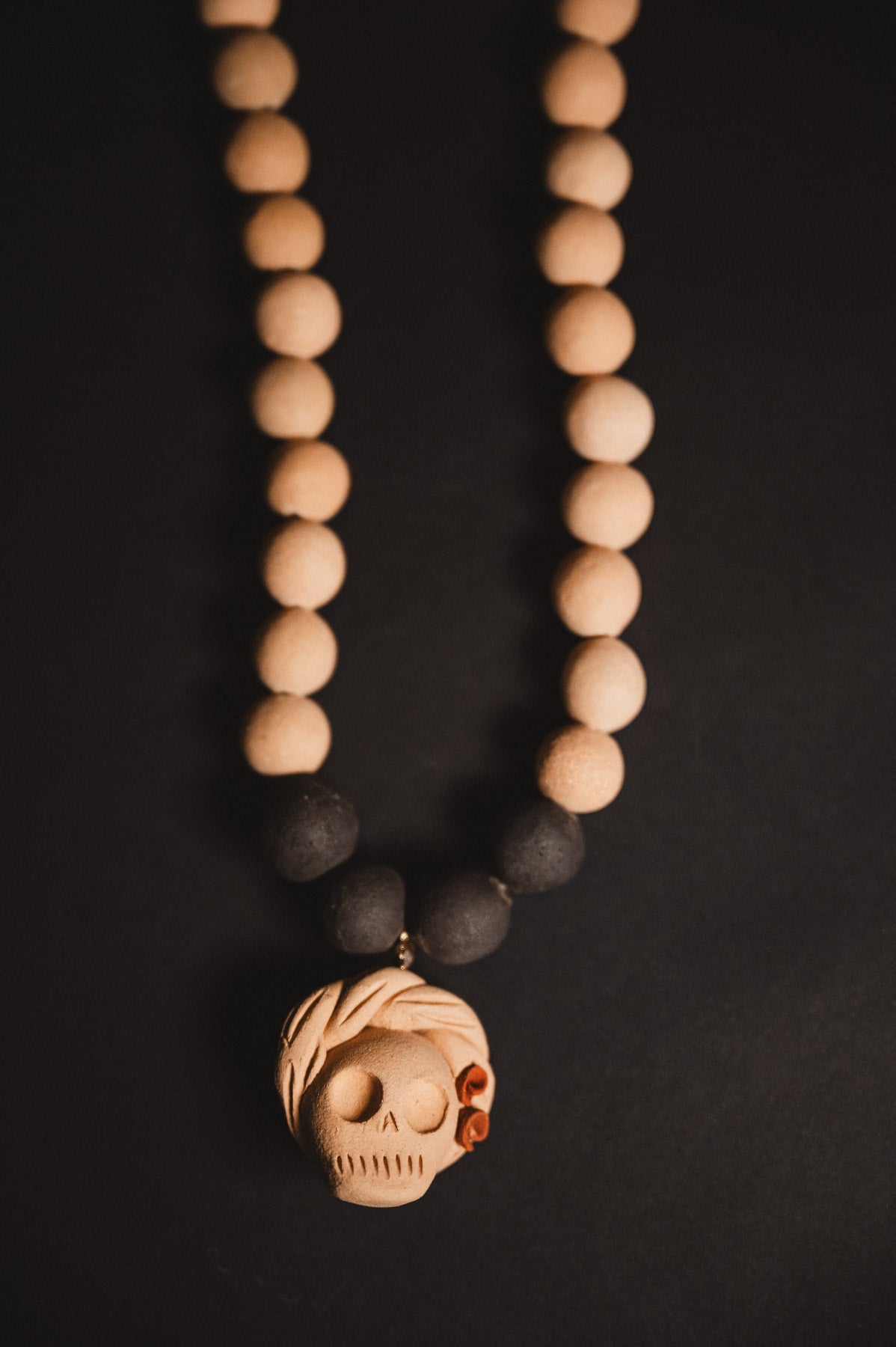 Necklace with wooden beads and a skull pendant on a dark background
