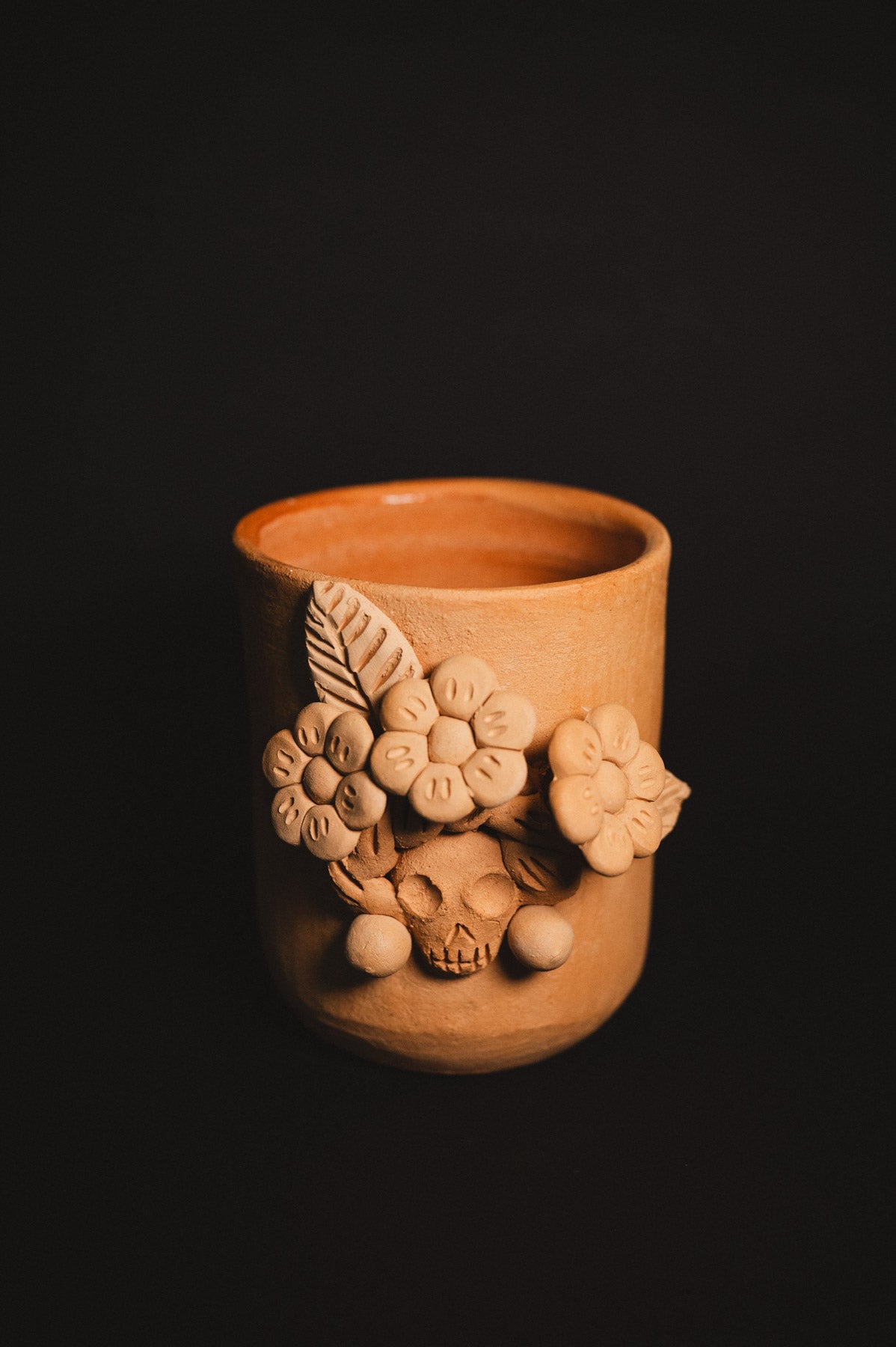 Terracotta cup with floral and skull designs on a black background