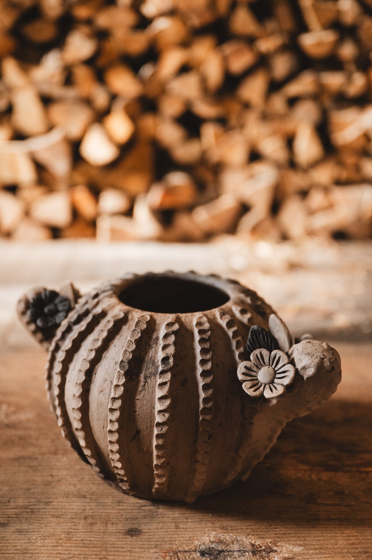 Ceramic cactus planter with floral design on a wooden surface with blurred woodpile background