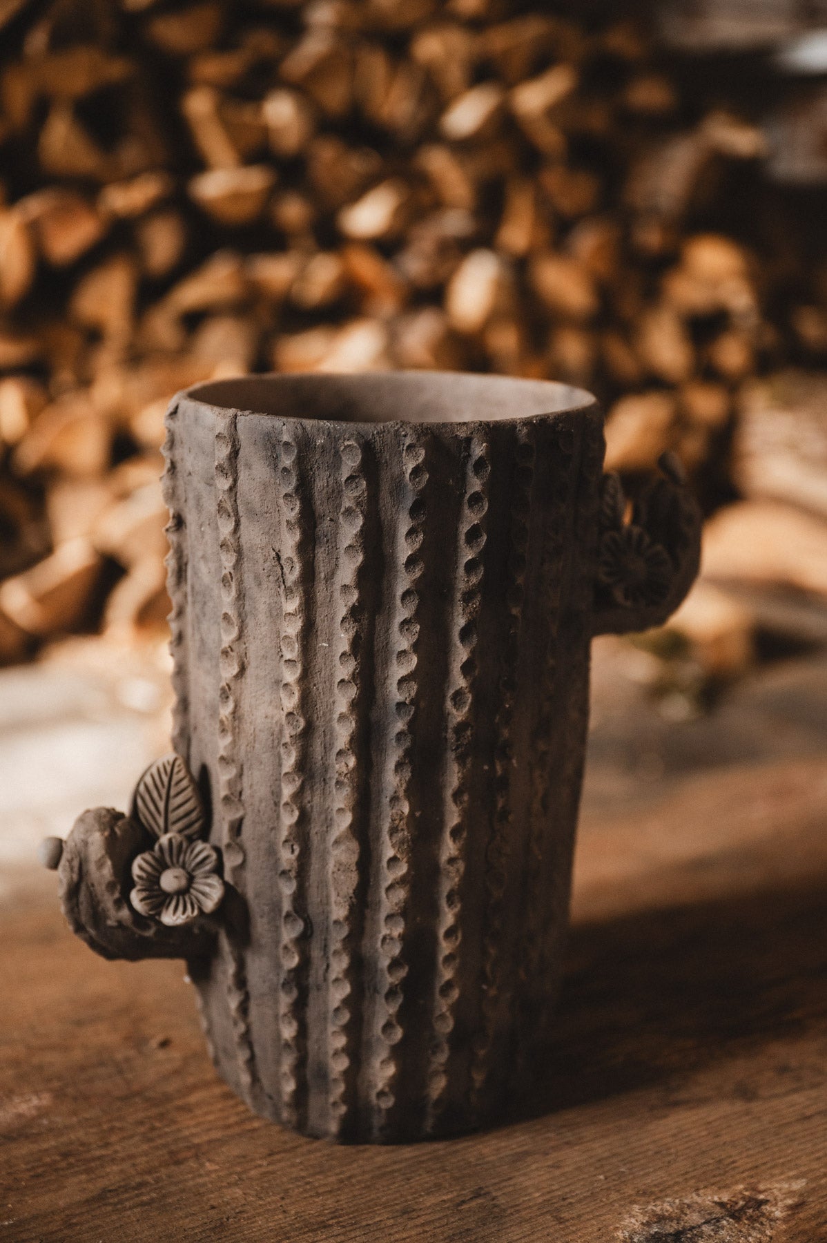 Ceramic cactus-shaped planter with textured design on a wooden surface with stacked firewood in the background.