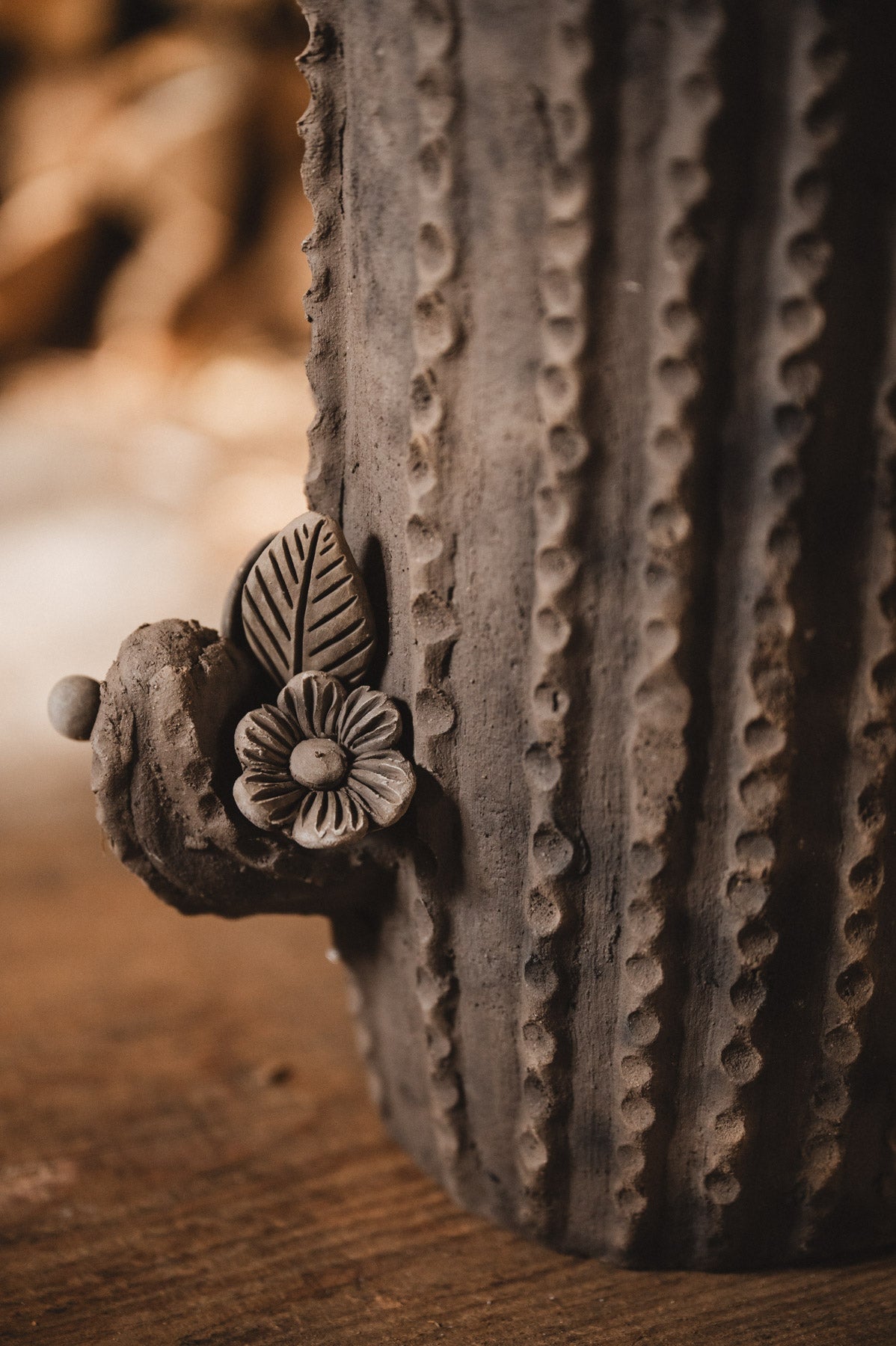 Ceramic cactus-shaped planter with textured design on a wooden surface with stacked firewood in the background.