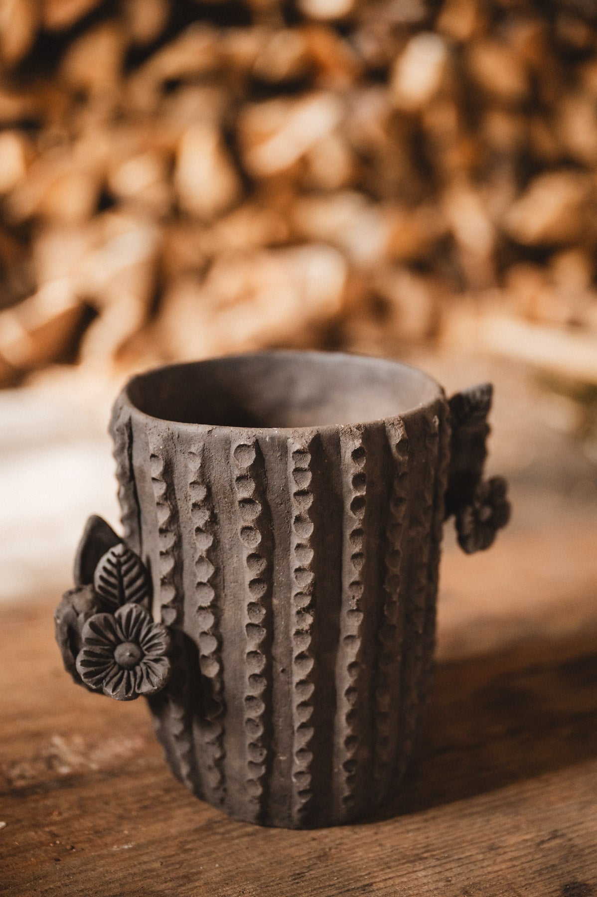 Ceramic cactus-shaped planter with textured design on a wooden surface with stacked firewood in the background.