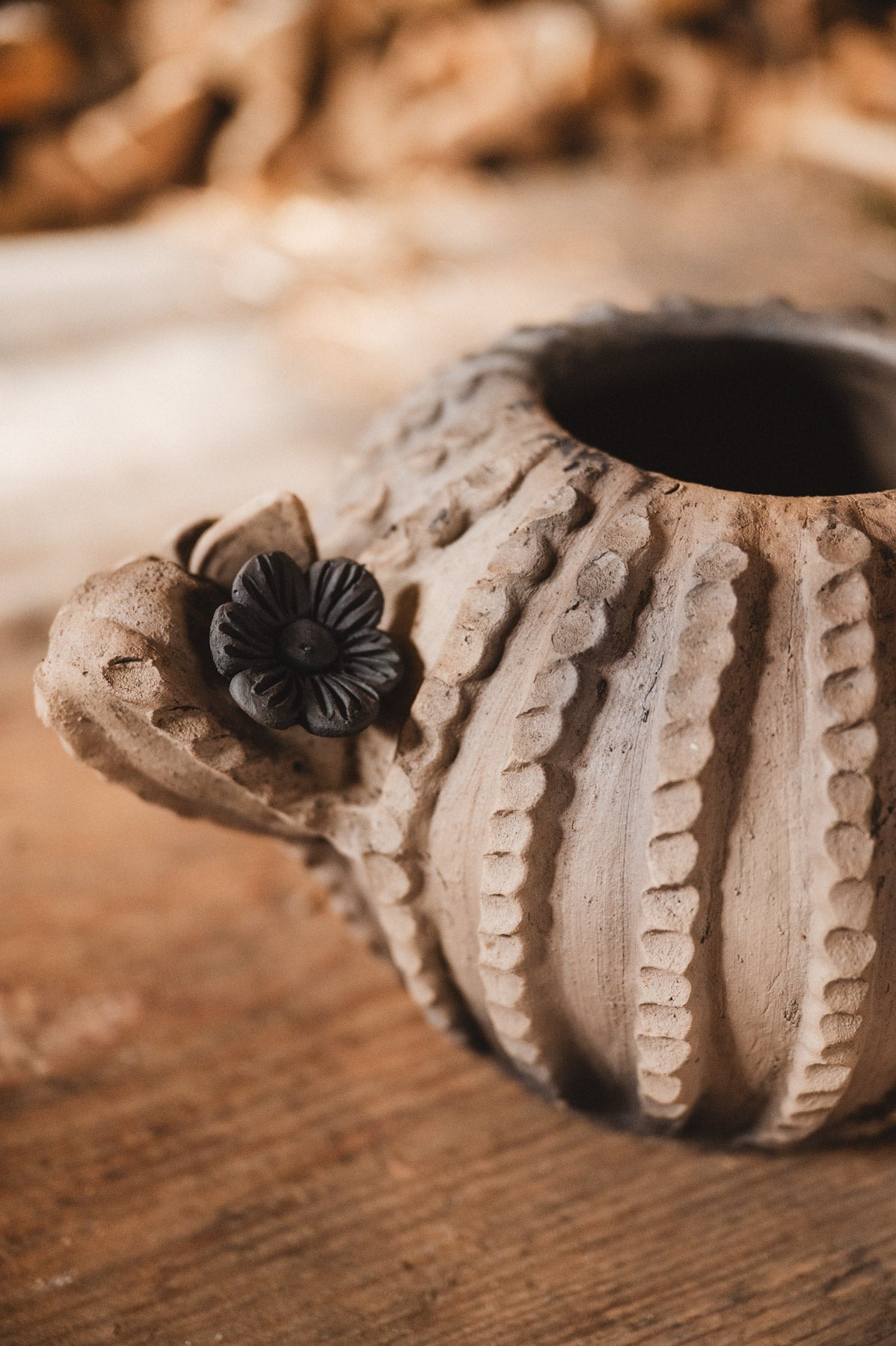 Ceramic cactus planter with floral design on a wooden surface with blurred woodpile background