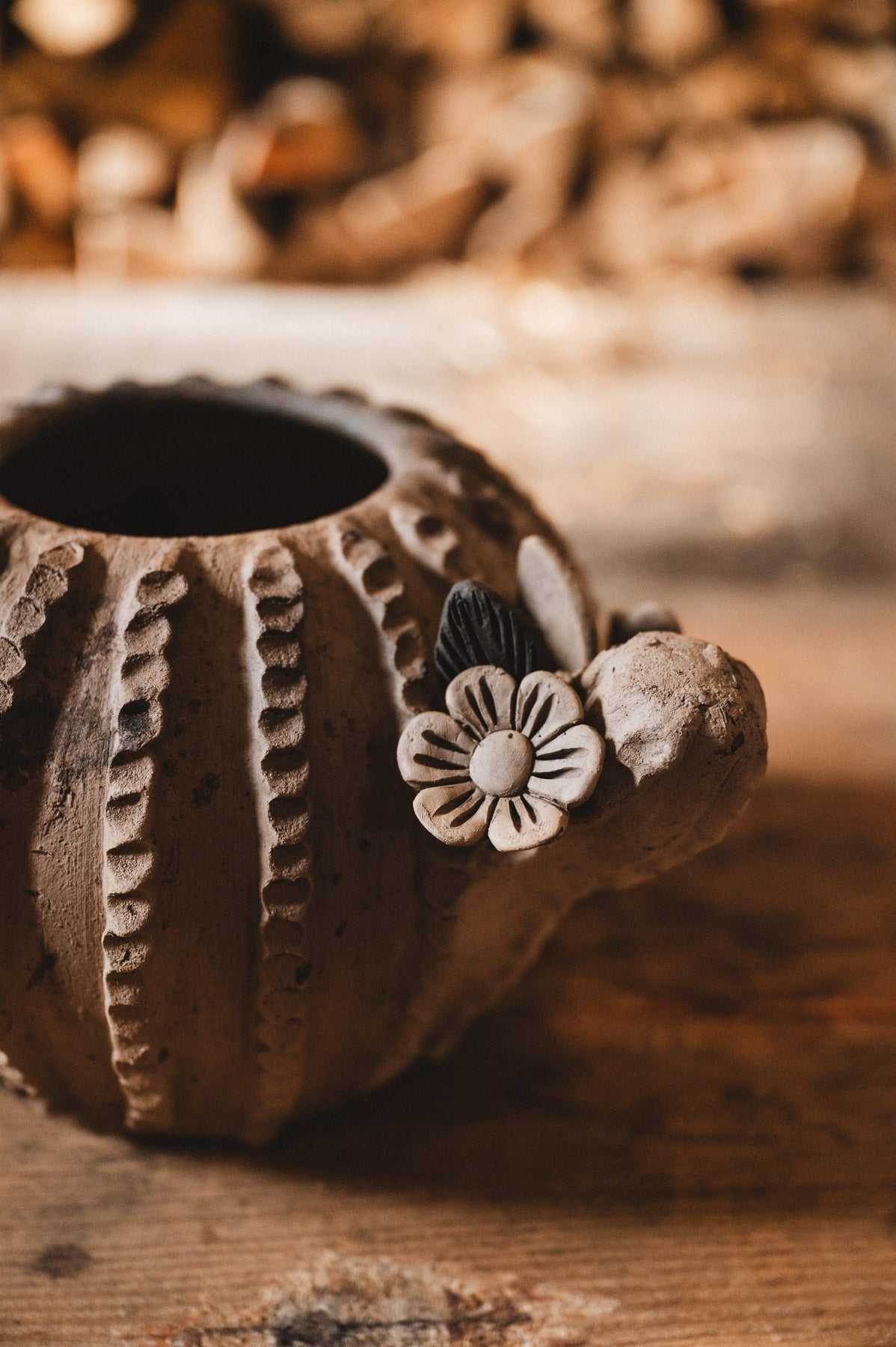 Ceramic cactus planter with floral design on a wooden surface with blurred woodpile background