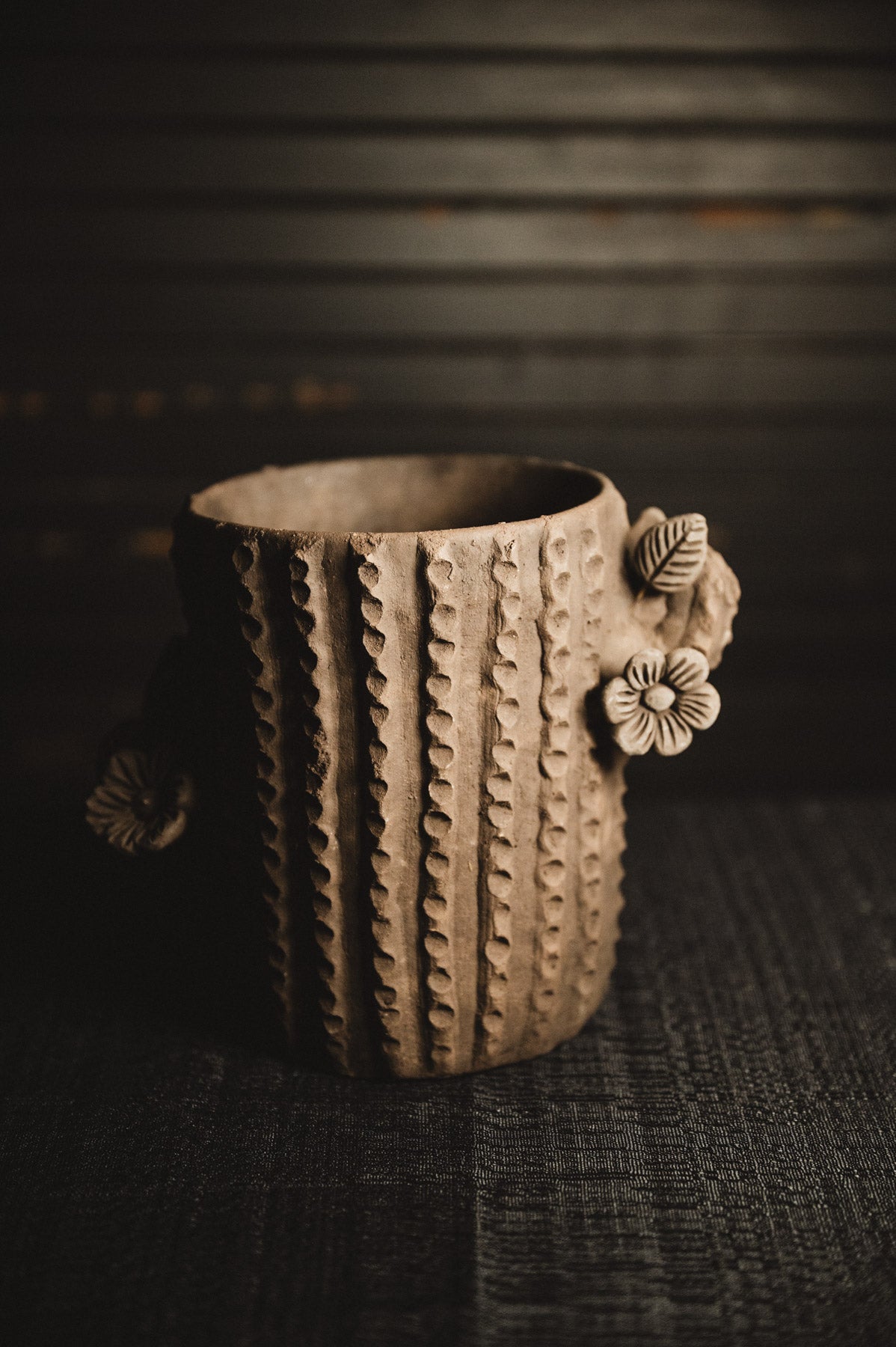 Ceramic planter with textured design and floral handle on a dark background