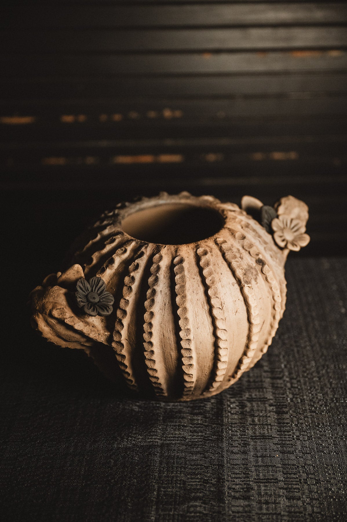 Ceramic planter with textured surface and floral decorations on a dark background