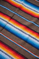 A close-up of a woven textile with diagonal stripes in brown, blue, white, yellow, orange, and red, showing a textured fabric pattern.