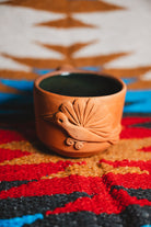 Terracotta cup with decorative design on a colorful patterned fabric background