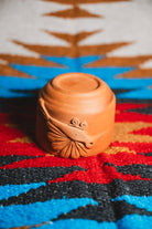 Terracotta pot with a face design on a colorful patterned fabric background