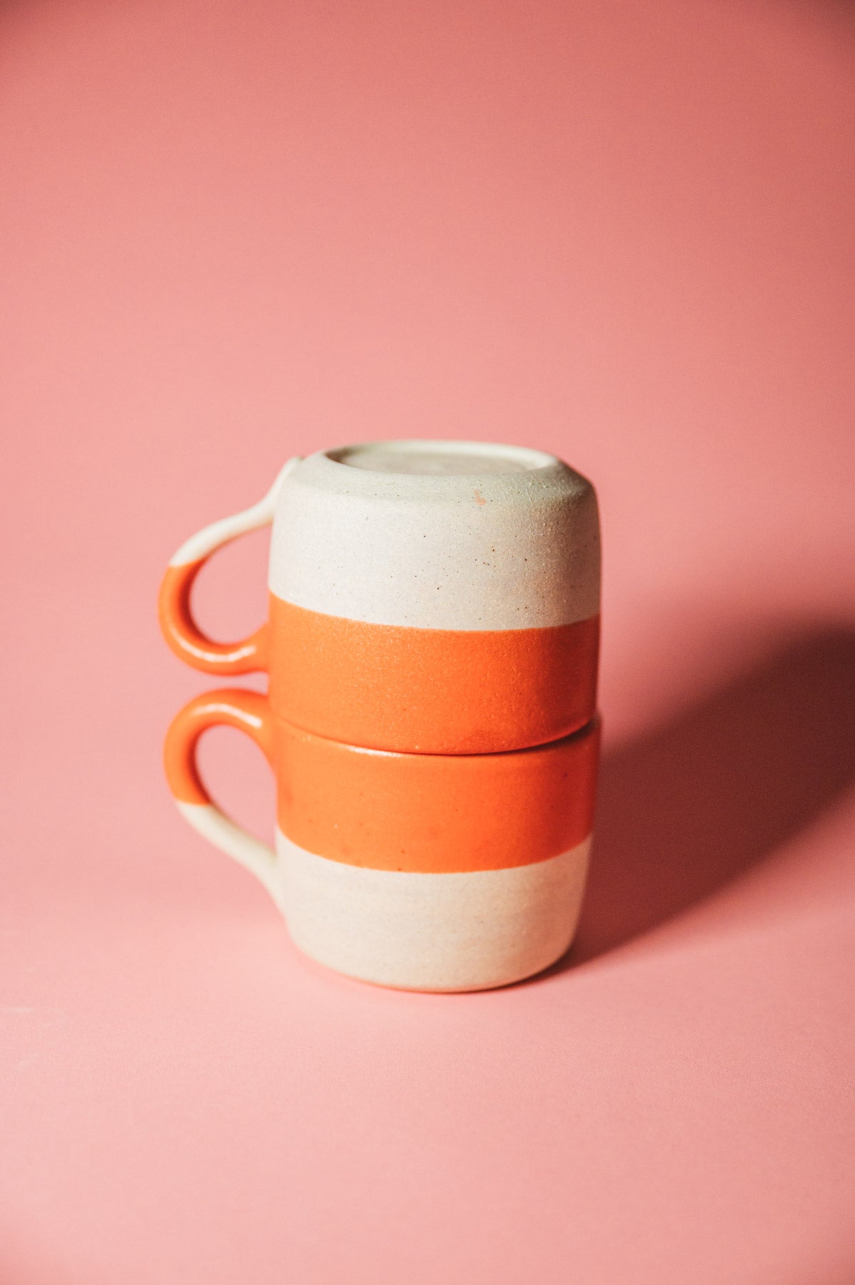 Stack of two ceramic mugs with orange and white design on a pink background