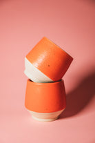 Two stacked ceramic pots with orange and white design on a pink background