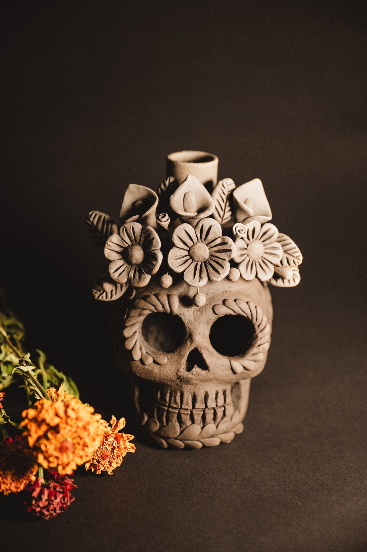 Ceramic skull vase with floral decorations on a dark background