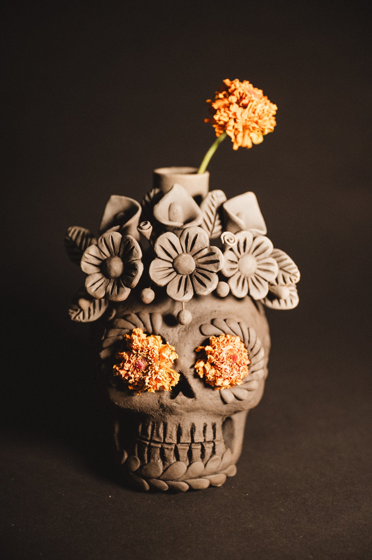 Ceramic skull vase with floral designs and orange flowers against a dark background