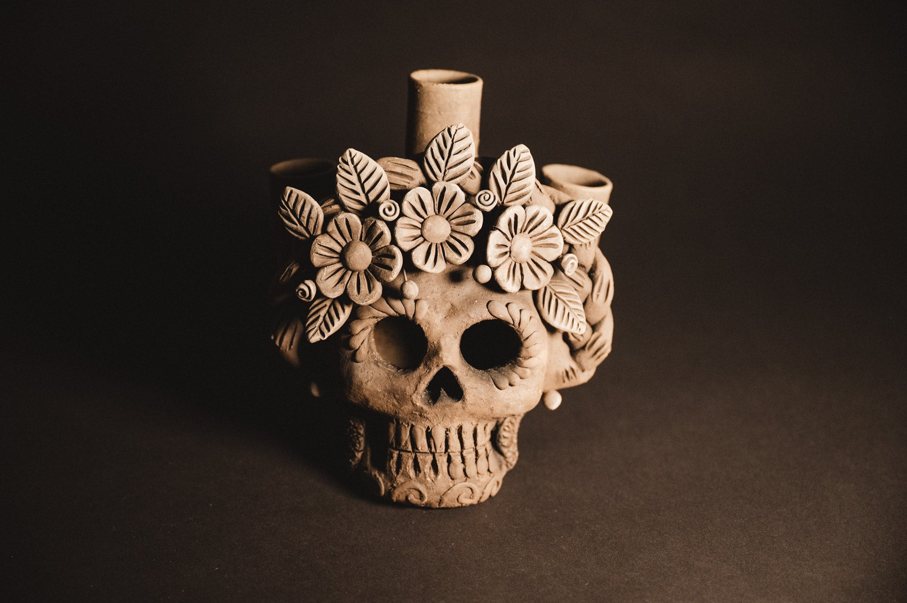 Ceramic skull vase with floral design on a dark background